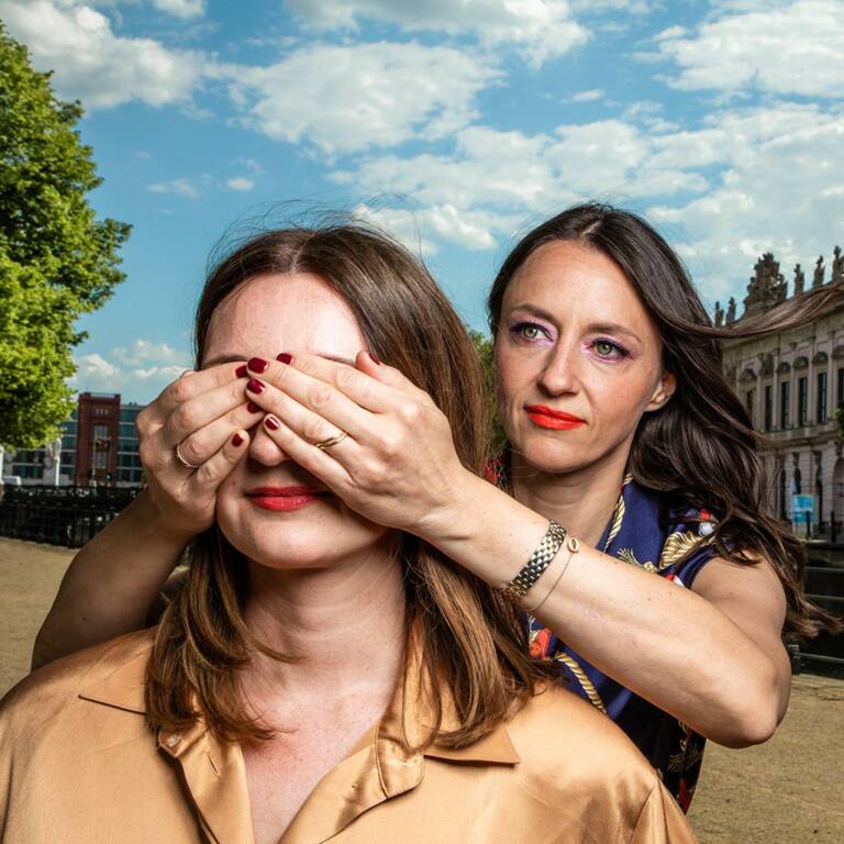 Woman holds her hands in front of another woman's eyes